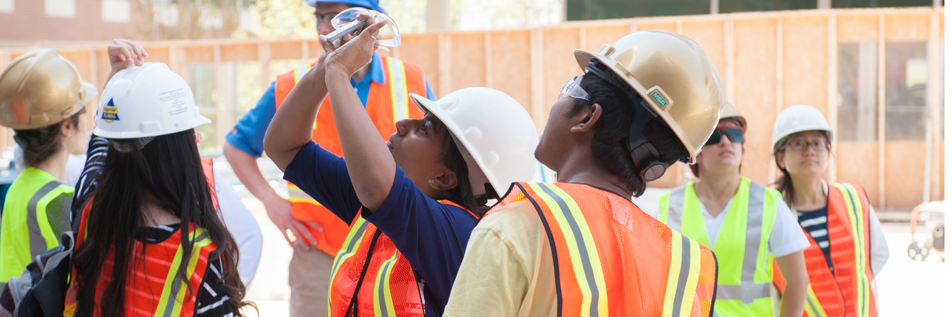 Male and female students observing images through device at construction site. 