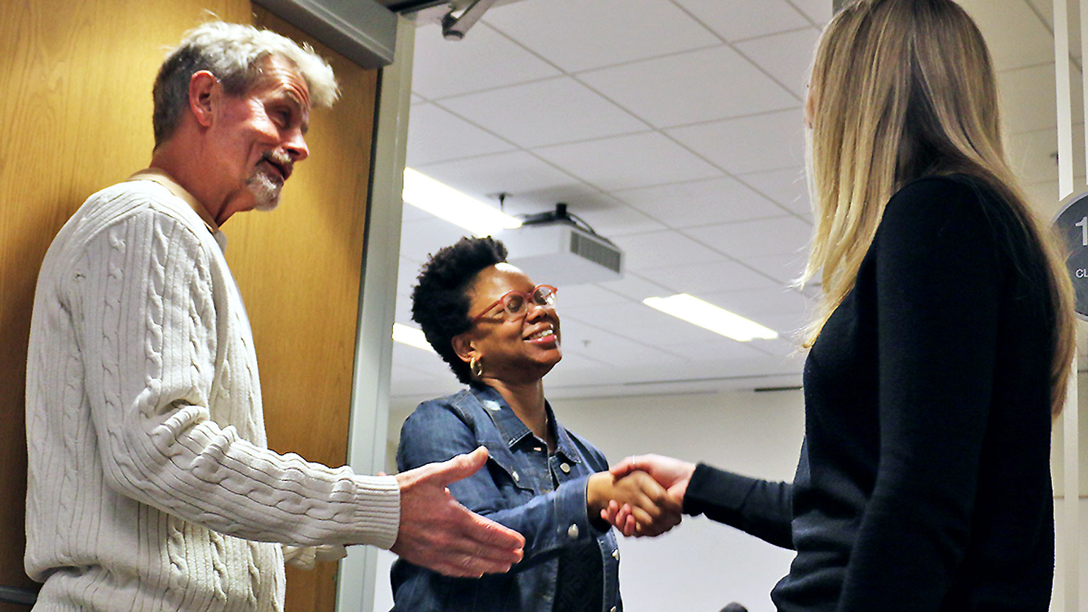 Two faculty members and a student shaking hands. 