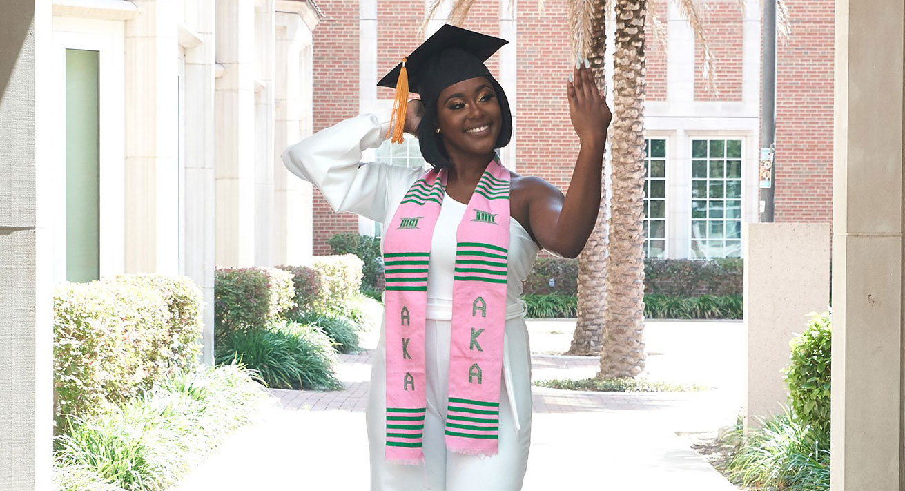 Charisse Spence posing outside dressed in cap and sorority scarf. 