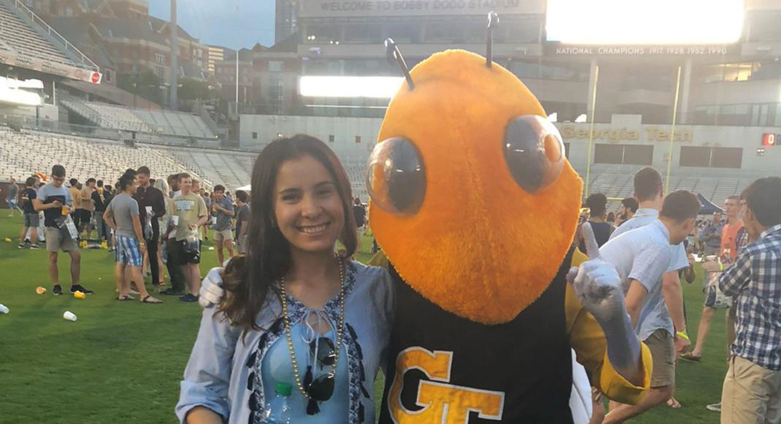 Monica Sierra standing with GT Buzz at on football field. 