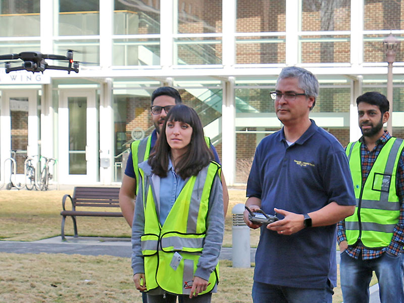 Professor and students analyzing a flying drone outside. 