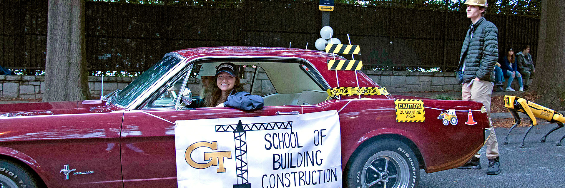 A student drives a Ford mustang in the Wreck Parade followed by a SPOT robot.