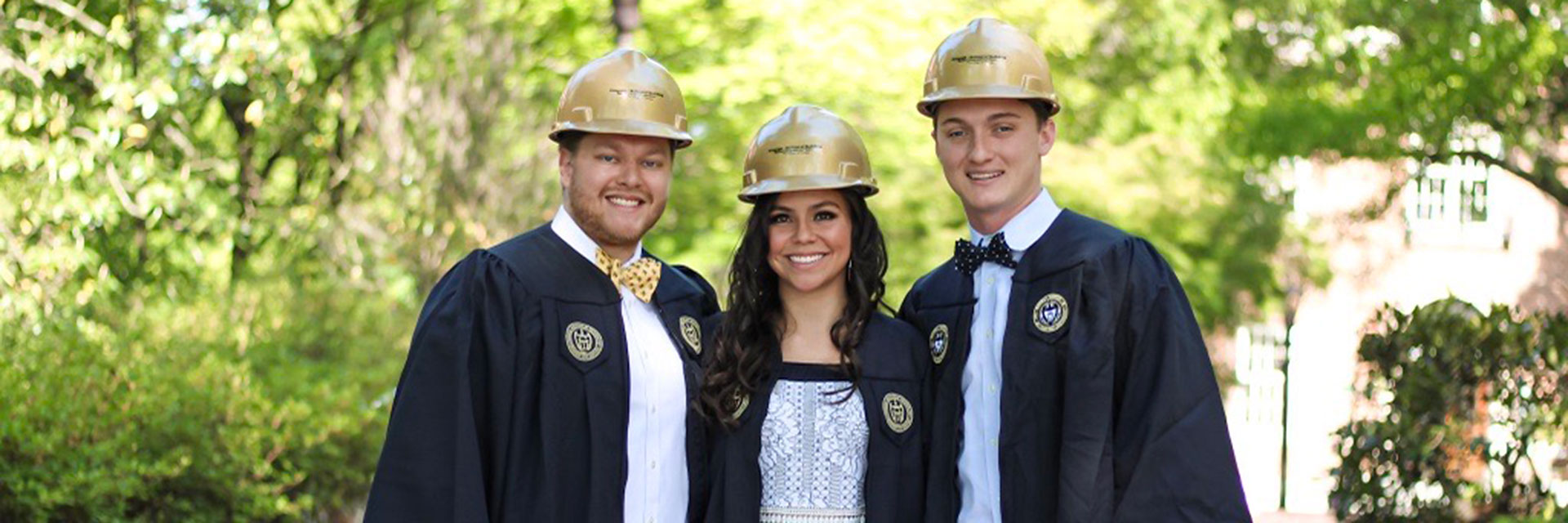Undergraduate students in graduation robes wearing hard hats.