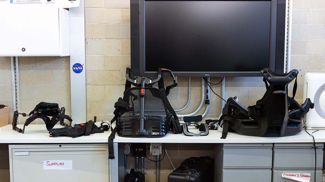 Three different types of wearable exoskeletons displayed on a cabinet.