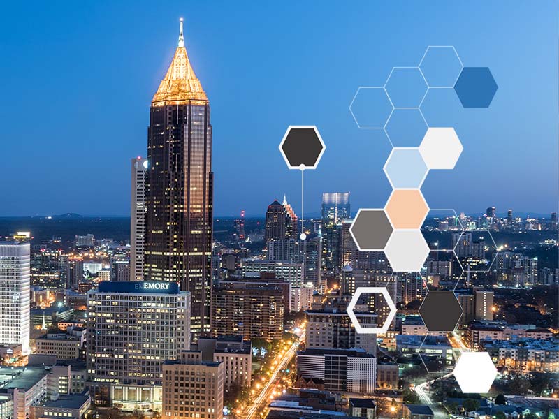A hive pattern in front of the Atlanta skyline at night.
