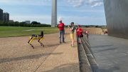 People taking photos of robot dog, with one leg of the Gateway Arch in the background